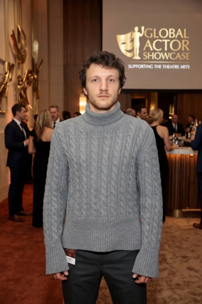 A young man wearing a grey turtleneck sweater standing in a formal event space at the Global Actor Showcase.