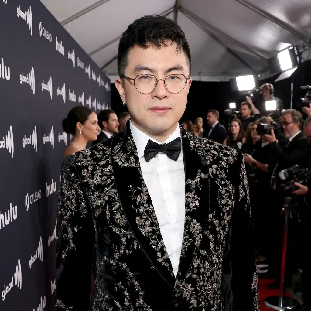 Actor Bowen Yang posing on the red carpet at a GLAAD event wearing a black velvet suit with intricate silver floral embroidery and a classic black bowtie