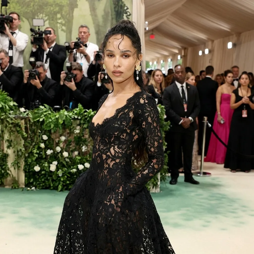 Zoe Kravitz posing on the Met Gala red carpet wearing a sheer black lace gown with a plunging neckline and floral earrings