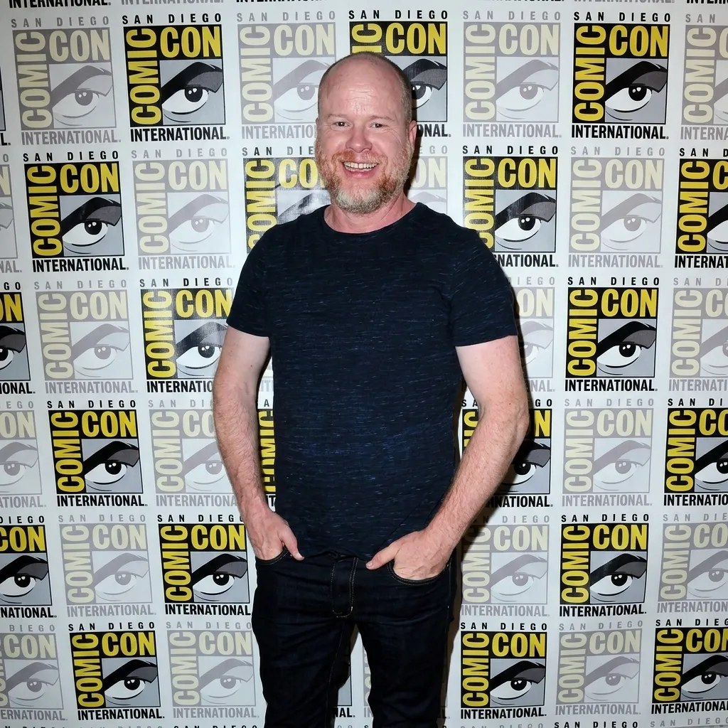 Director Joss Whedon smiling on the press line against the official San Diego Comic-Con International logo backdrop.