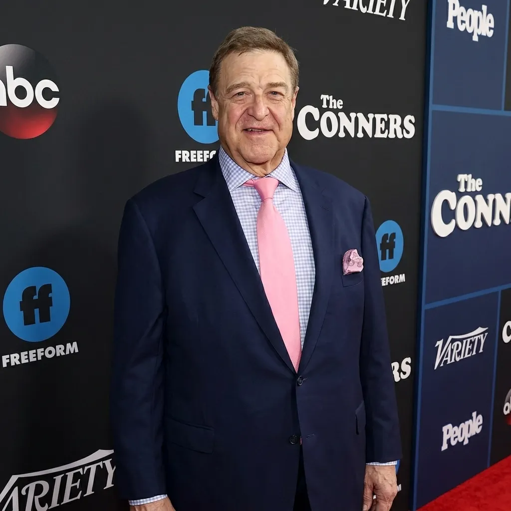 Actor John Goodman wearing a navy blue suit and pink tie on the red carpet for The Conners television show event