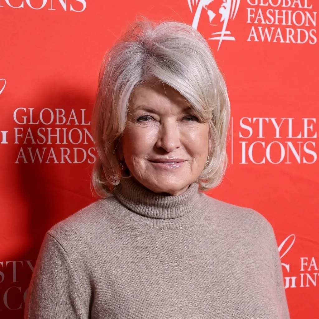 Martha Stewart wearing a beige turtleneck sweater in front of a red Global Fashion Awards backdrop.