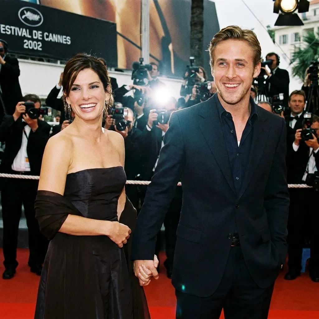 Sandra Bullock in a black strapless dress and Ryan Gosling in a dark suit holding hands and smiling on the red carpet at the 2002 Cannes Film Festival.