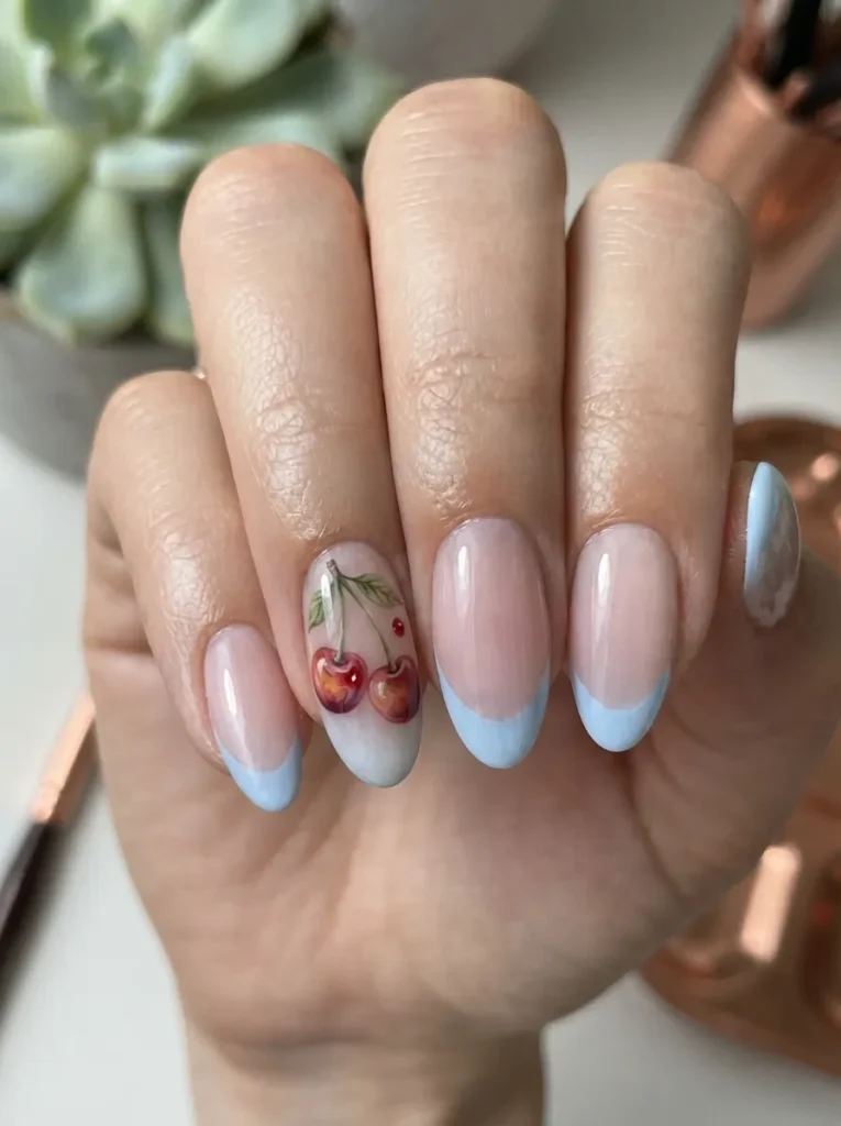 Close-up of a hand showcasing almond-shaped nails with baby blue French tips and an accent nail featuring detailed, realistic 3D-style cherry art with leaves.