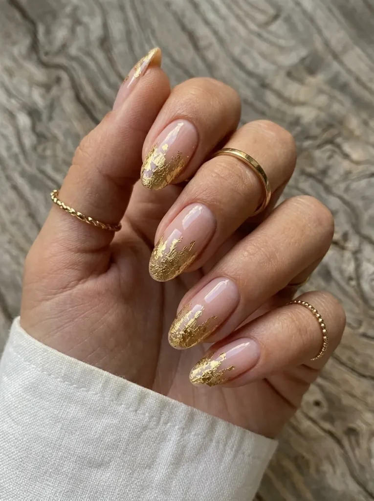 Nude almond nails featuring textured torn gold foil tips