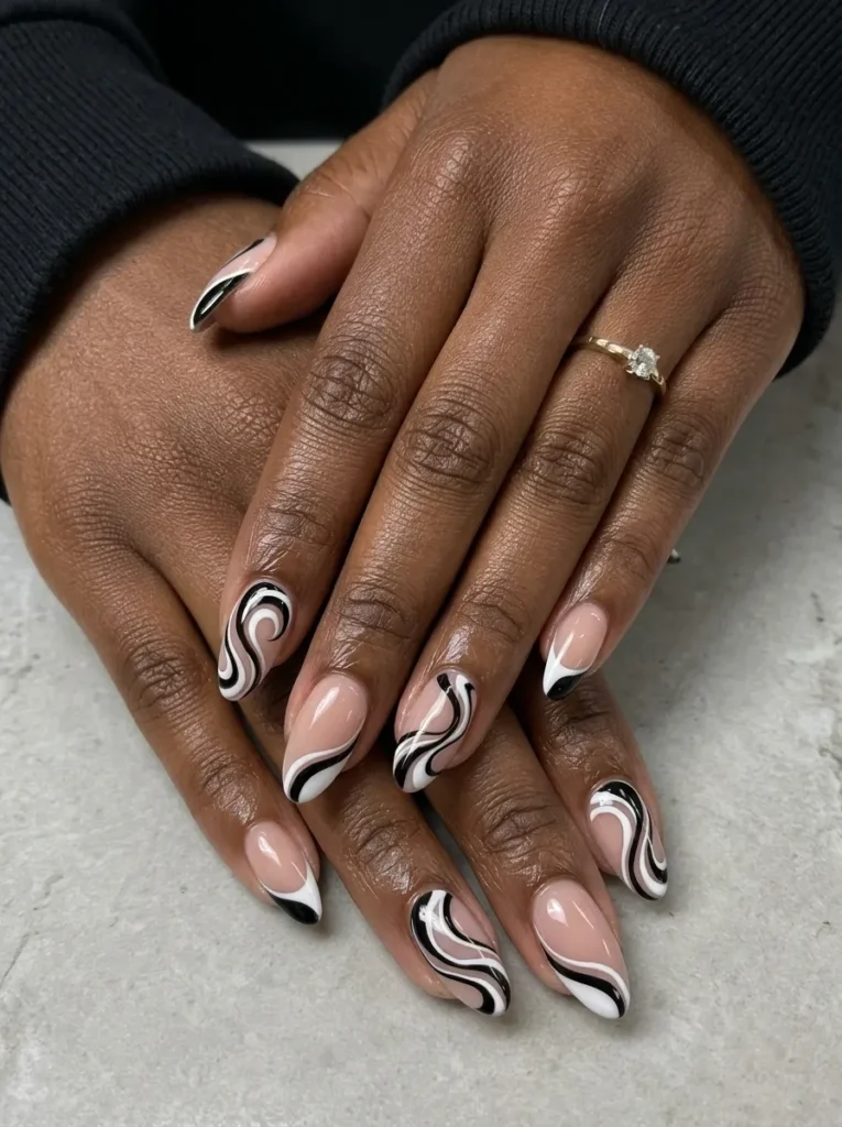 Almond-shaped nails designed with a nude base and bold, abstract black and white swirls