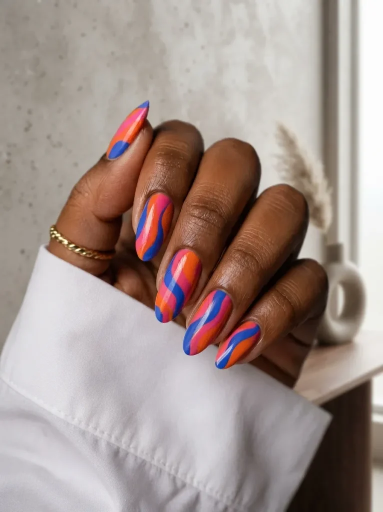 Almond-shaped nails featuring a vibrant abstract wave pattern in shades of bright pink, royal blue, and orange