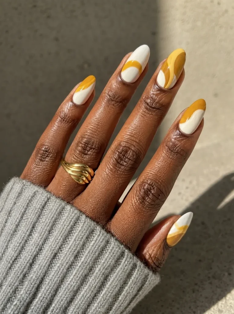 Almond-shaped nails with a white base and mustard yellow abstract swirls and color-blocking