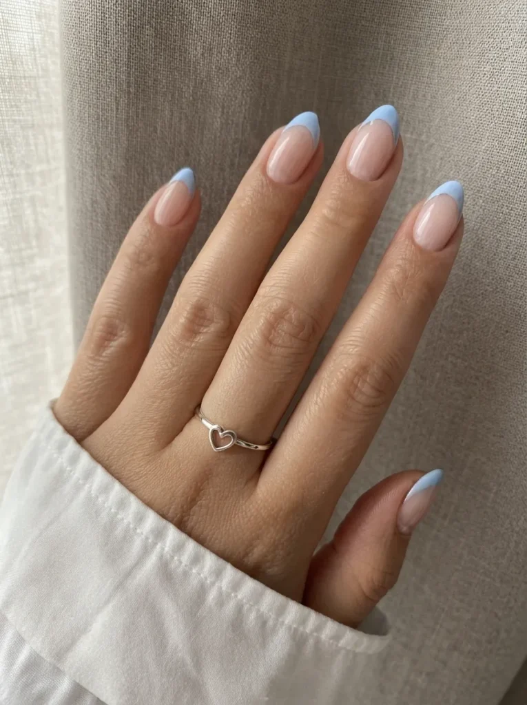 Almond-shaped nails with light blue French tips and a heart ring