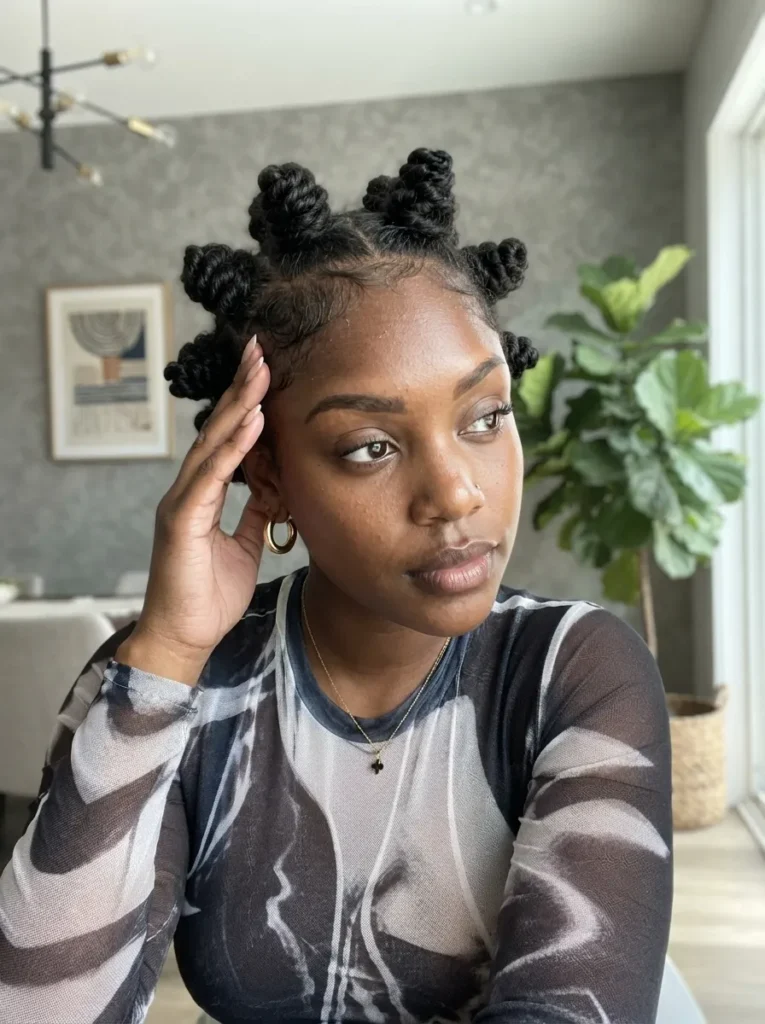 Young Black woman with Bantu knots, neatly laid edges, and gold hoop earrings, wearing a black and white patterned sheer top