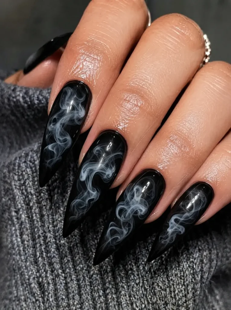 Close-up of black stiletto nails featuring intricate white smoke art against a grey knit background