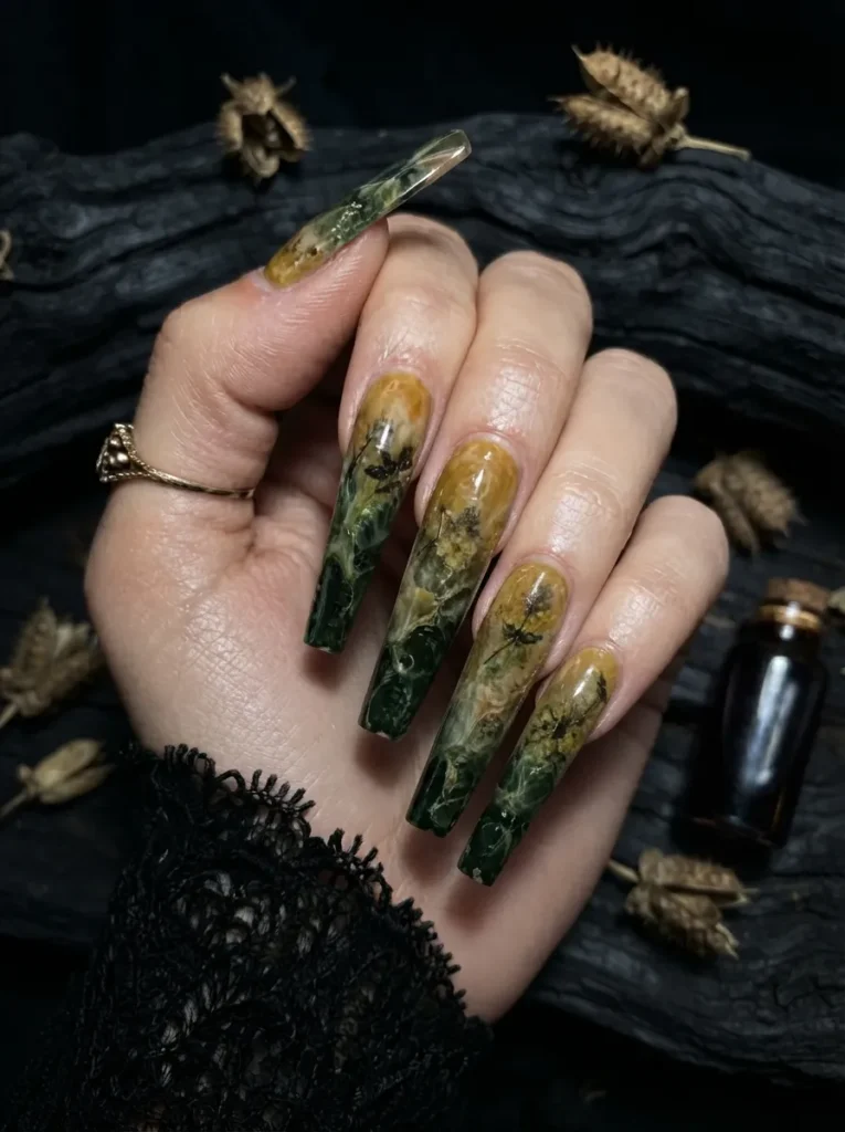 Extra-long coffin nails showcasing an amber and dark green botanical encapsulation design with pressed herbs and foliage.