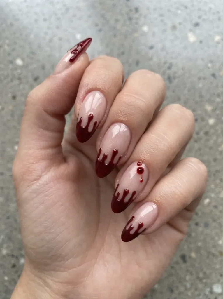 Almond-shaped nude nails styled with burgundy French tips that transition into dramatic, dripping blood designs and scattered 3D droplets.