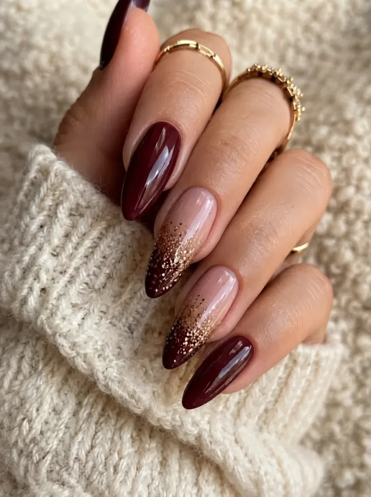 Burgundy almond nails styled with a gold glitter ombre gradient effect.