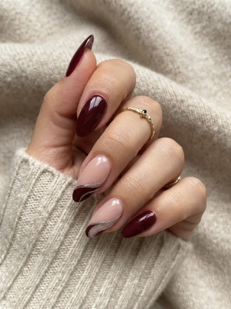 Burgundy almond nails adorned with nude and silver swirl accent art.