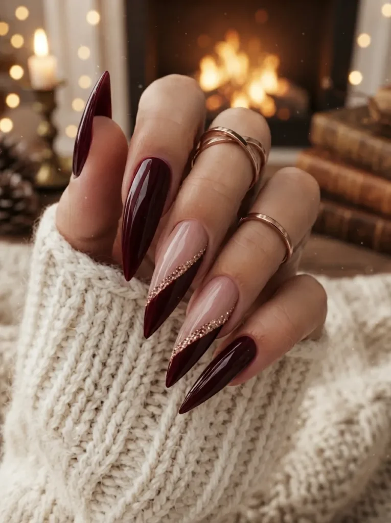 Burgundy and nude stiletto nails styled with rose gold glitter diagonal tips and rings.