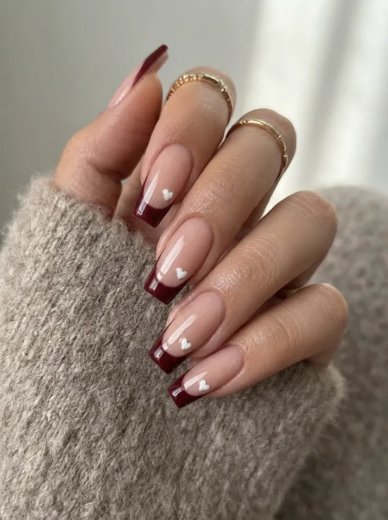 Burgundy french tip coffin nails embellished with tiny white 3D hearts.