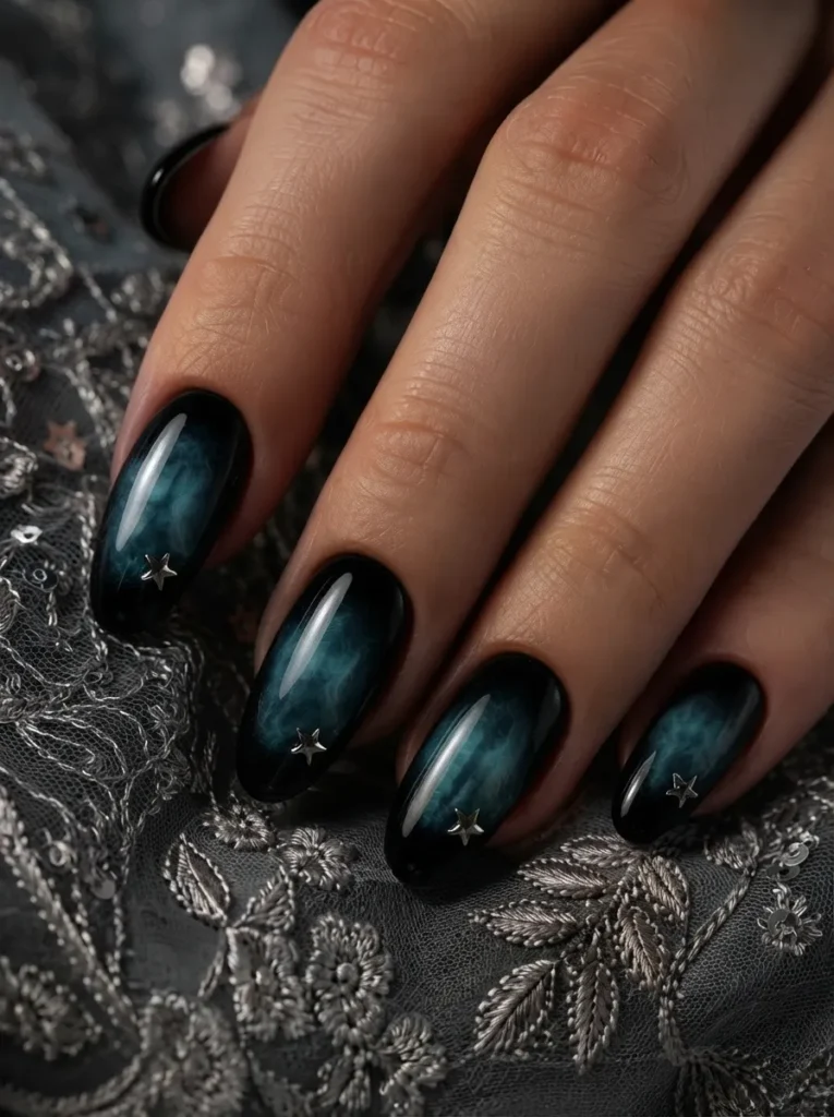 Hand displaying dark teal smoke-effect almond nails adorned with small star studs over lace fabric
