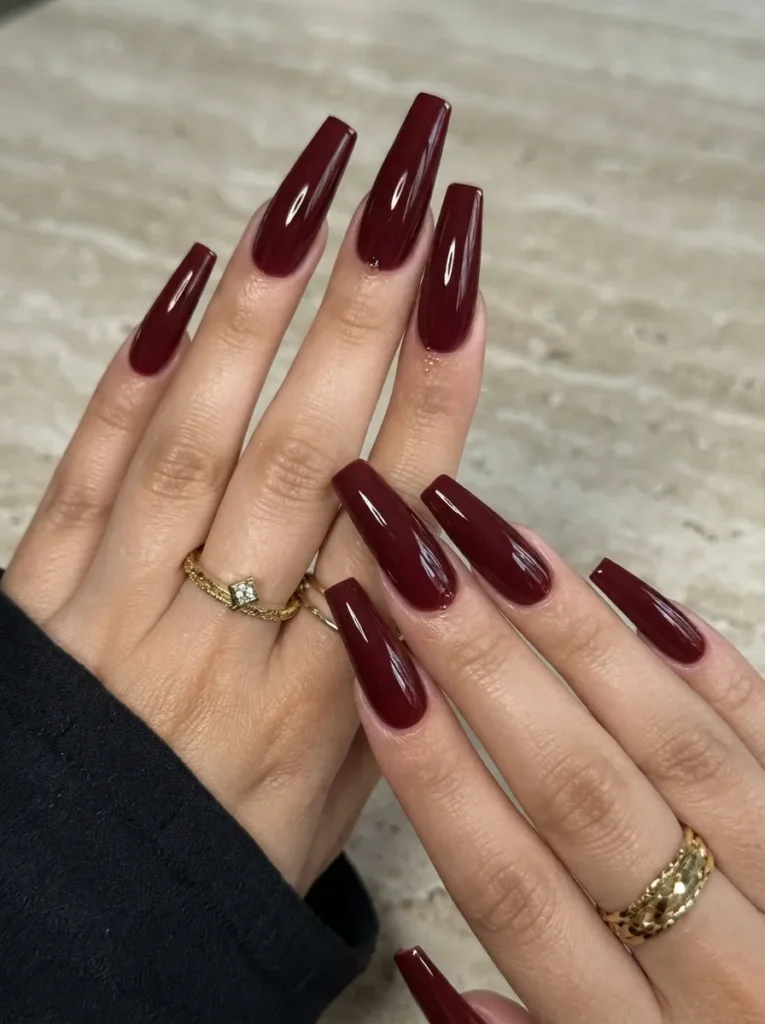 Glossy burgundy long coffin nails paired with gold rings.