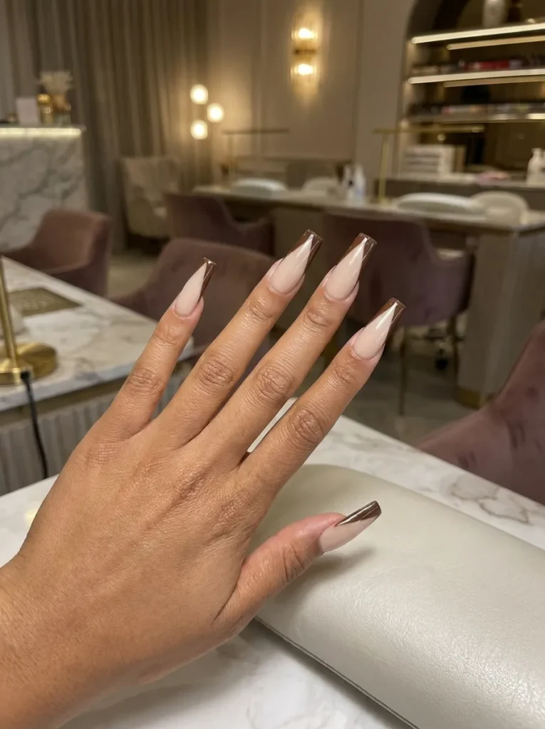 Long coffin-shaped nails featuring a neutral nude base with modern chocolate brown diagonal French tips