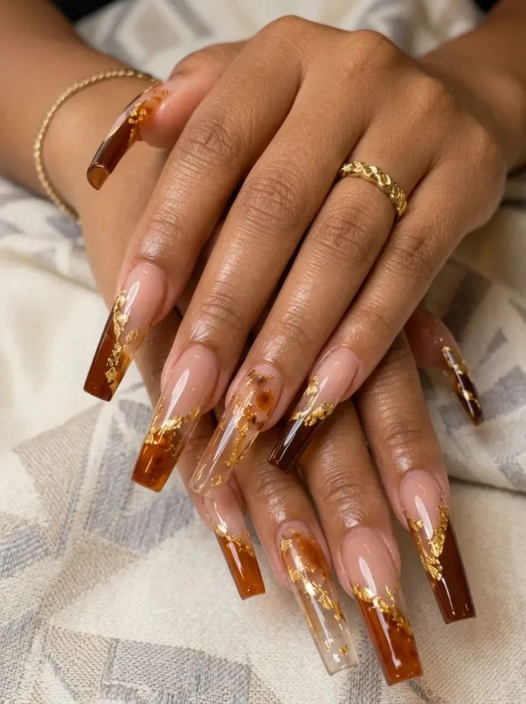 Hands wearing long square amber glass nails embellished with sparkling gold foil flakes