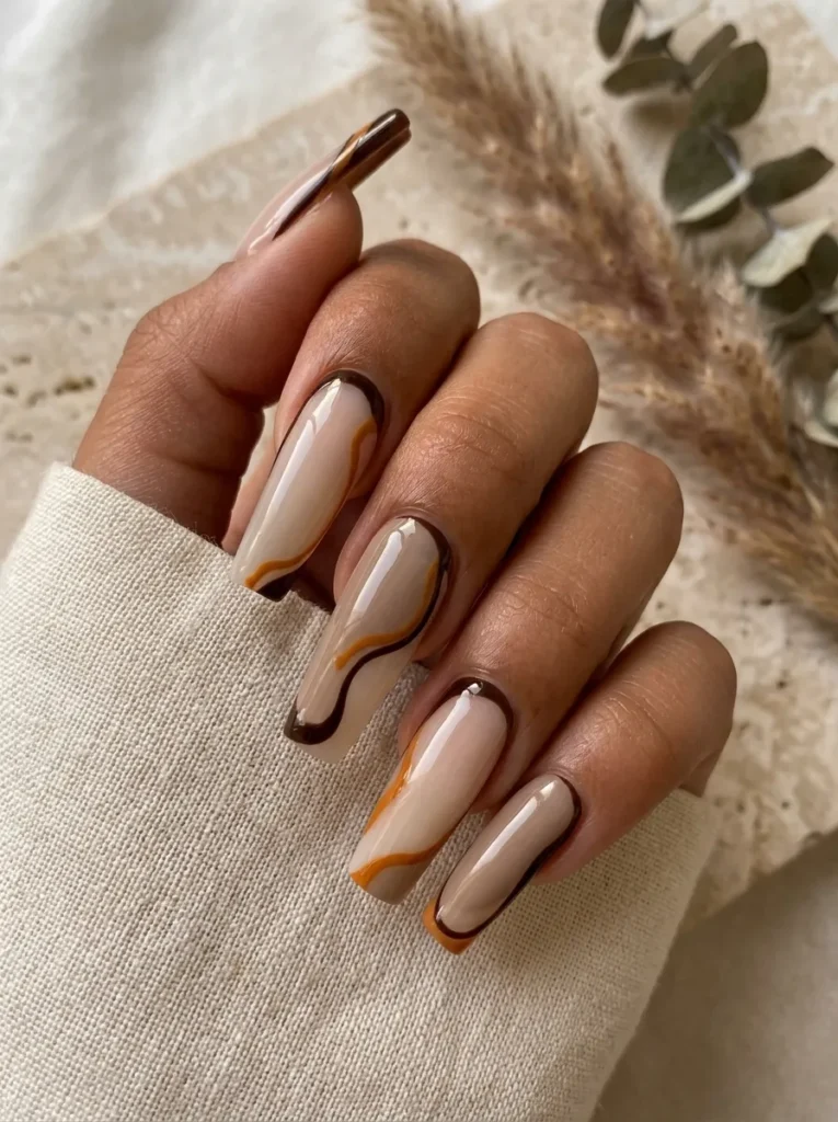 Hand wearing a cream sleeve showcasing long square nude nails styled with brown and amber swirl lines.