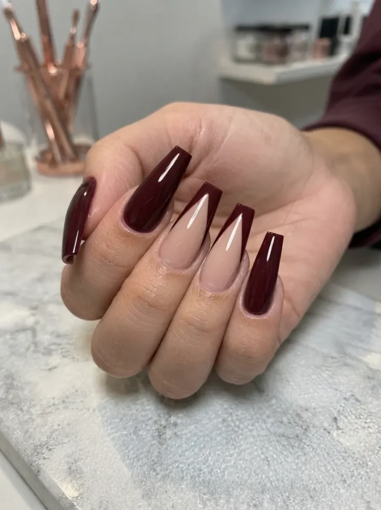 Long coffin nails featuring a mix of solid burgundy polish and deep V-french tips.