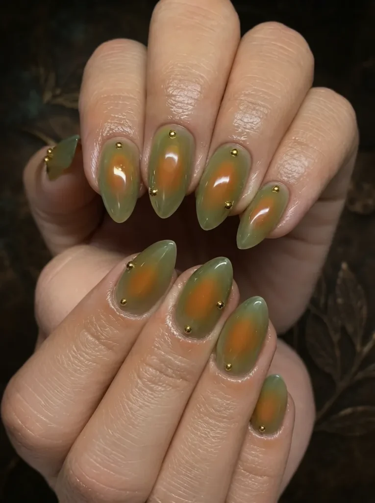 Close-up of olive green and orange aura nails decorated with small gold studs