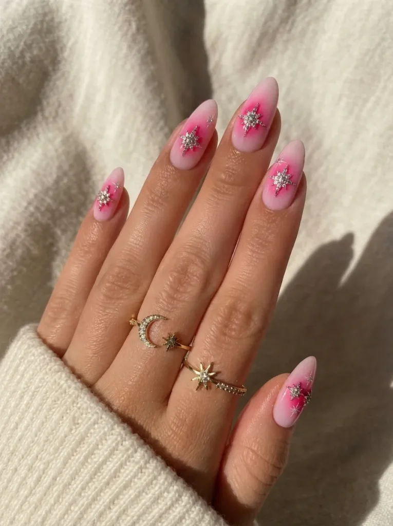 Hand displaying pink aura almond-shaped nails adorned with celestial crystal star and moon rings