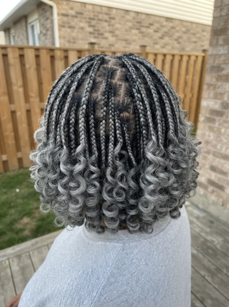 Back view of a person with short, shoulder-length box braids that transition from black roots to a mix of gray and silver with curly ends