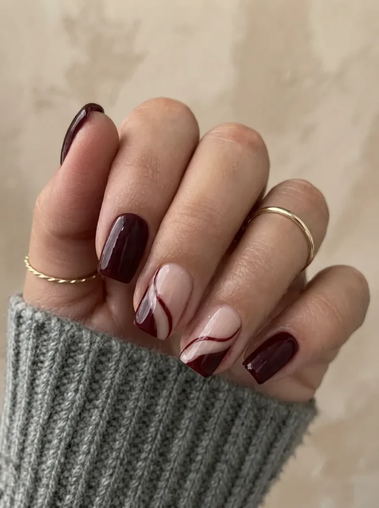 Short square burgundy nails paired with nude and deep red swirl accent art.