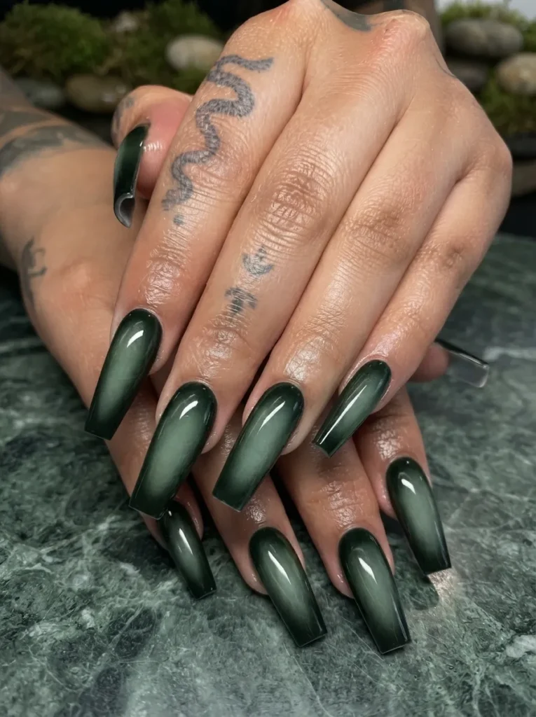 Hands showcasing smoky green cat-eye coffin-shaped nails with subtle finger tattoos