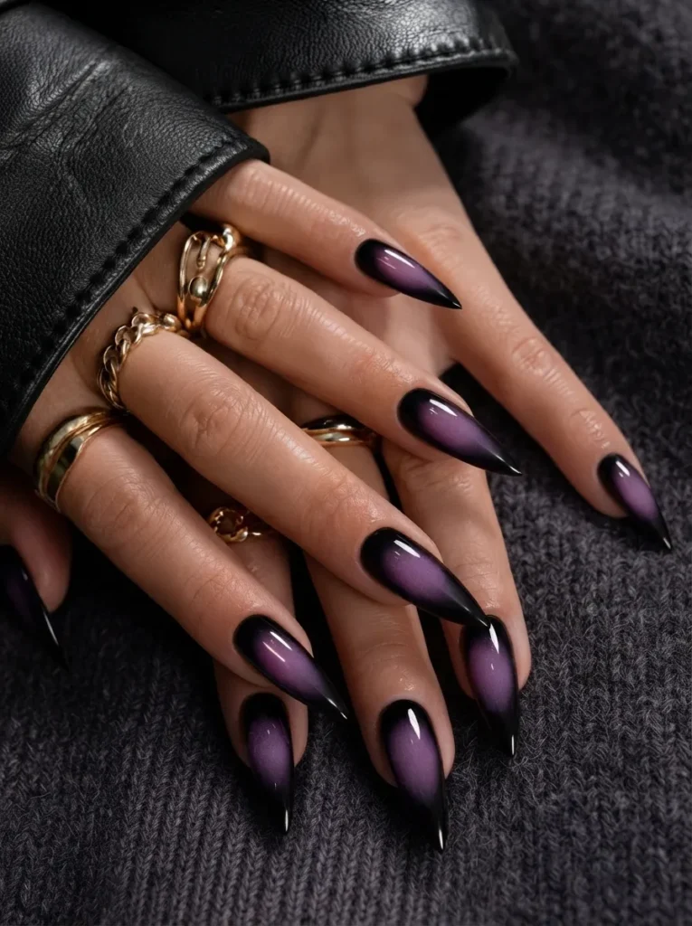Hands featuring smoky purple stiletto cat-eye nails accessorized with chunky gold rings