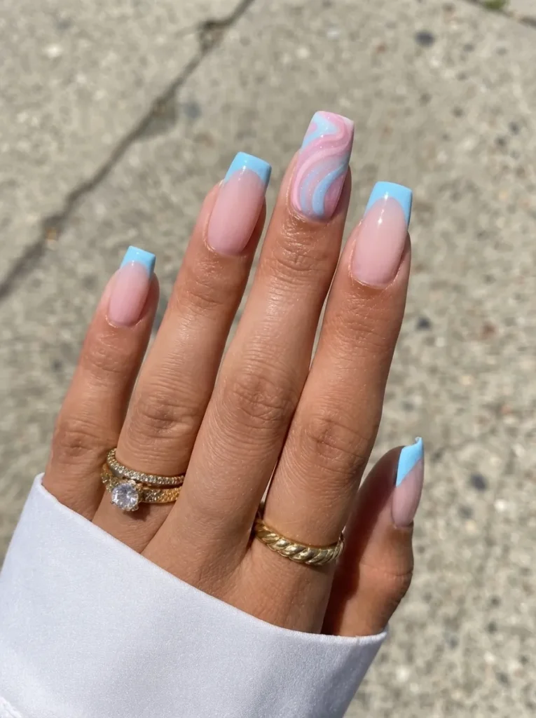 Square-shaped nails with light blue French tips and a pink and blue swirl accent nail, worn with gold rings.