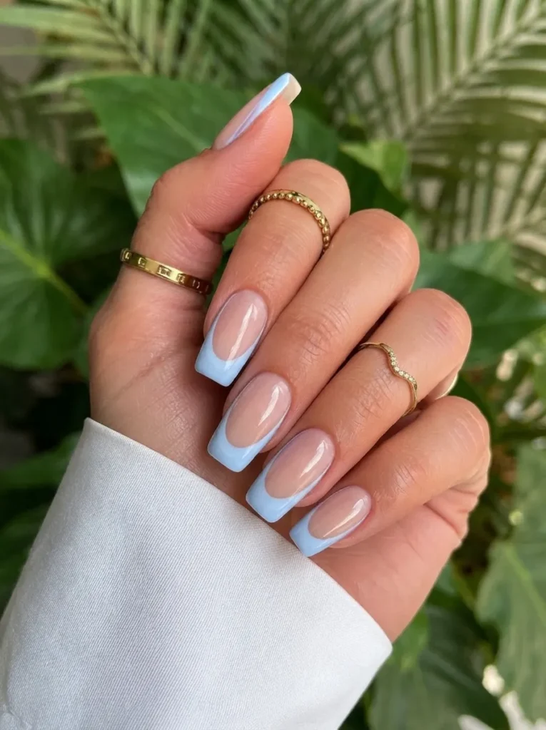 Square-shaped nails with classic light blue French tips, complemented by elegant gold rings.