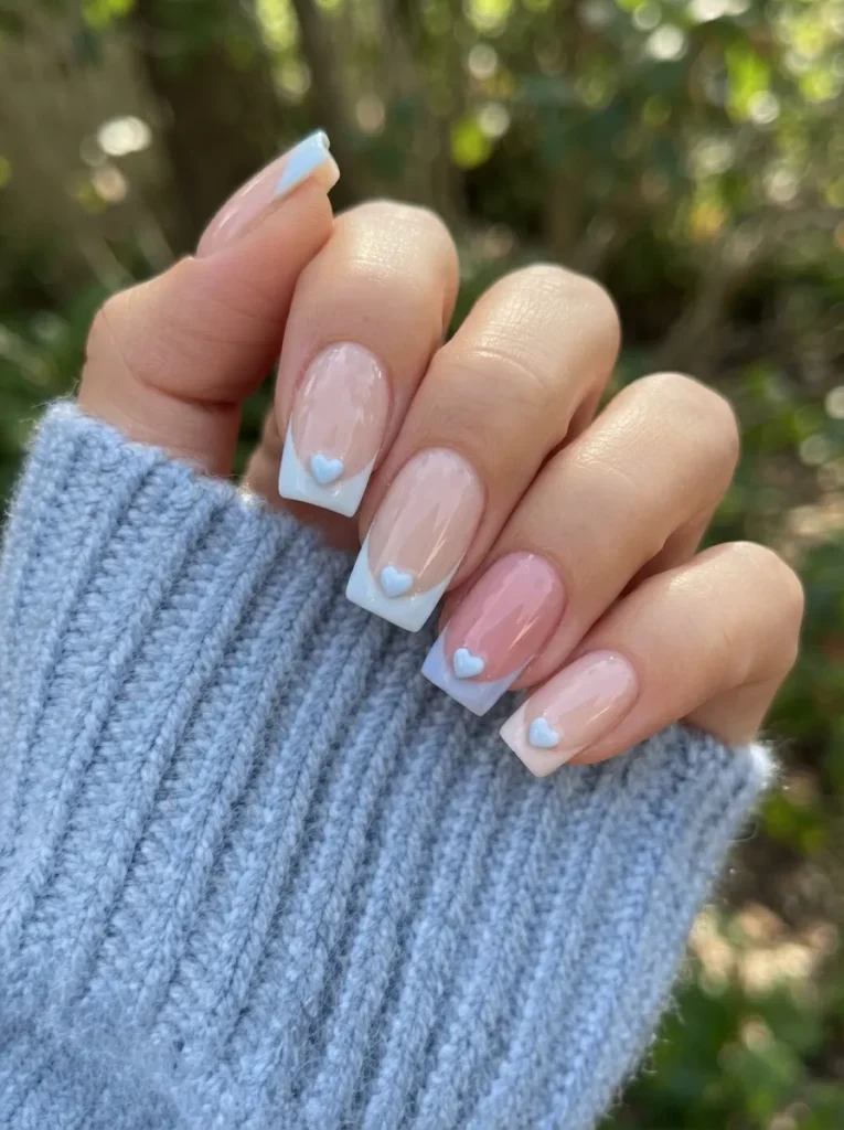 Square-shaped nails featuring light blue French tips and small 3D heart accents on each finger.