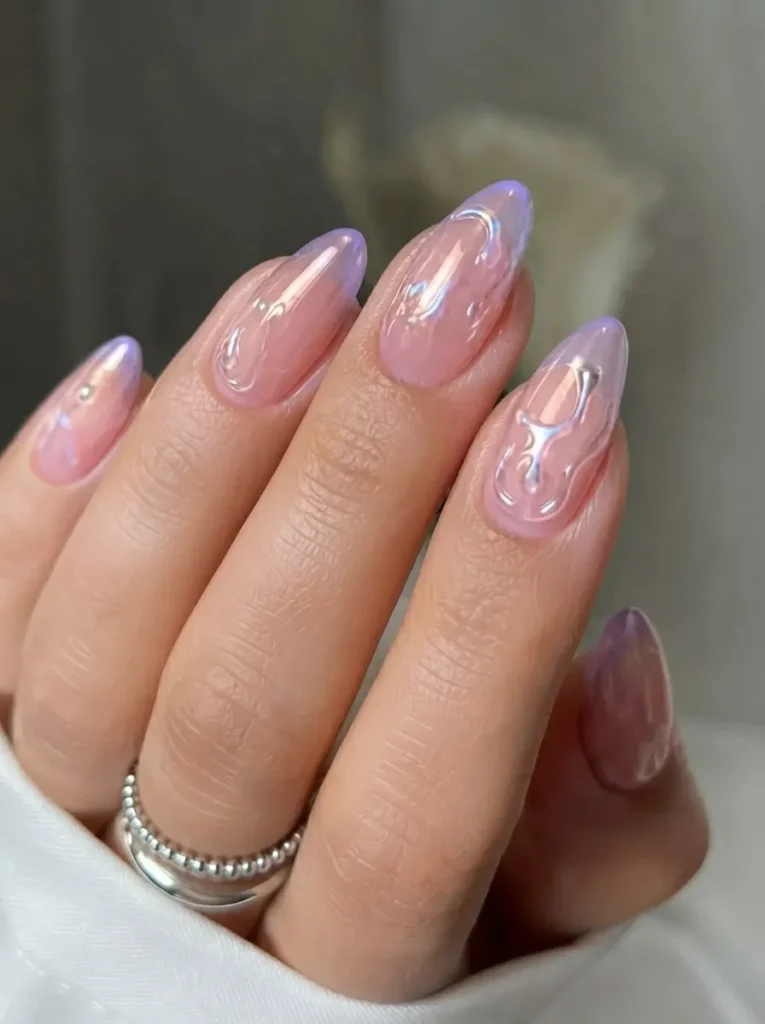 Close-up of translucent pink almond-shaped nails with 3D liquid metal chrome swirl accents and silver rings.